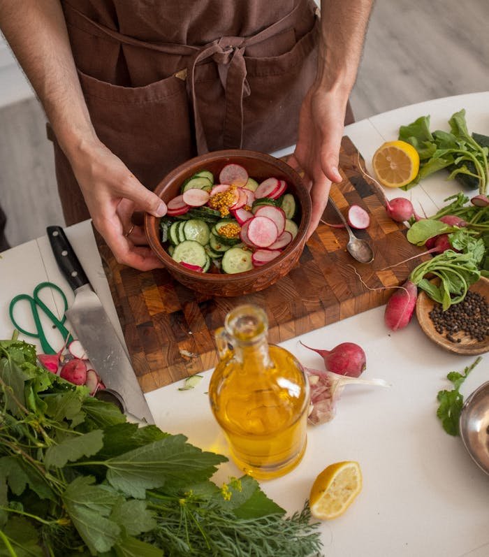 Chef prepares a fresh vegetable salad with radishes, cucumbers, and olive oil on a wooden board.