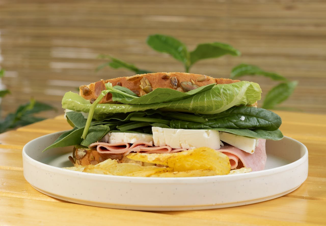 Mouthwatering sandwich with fresh spinach, ham, cheese, and crispy chips on a plate.